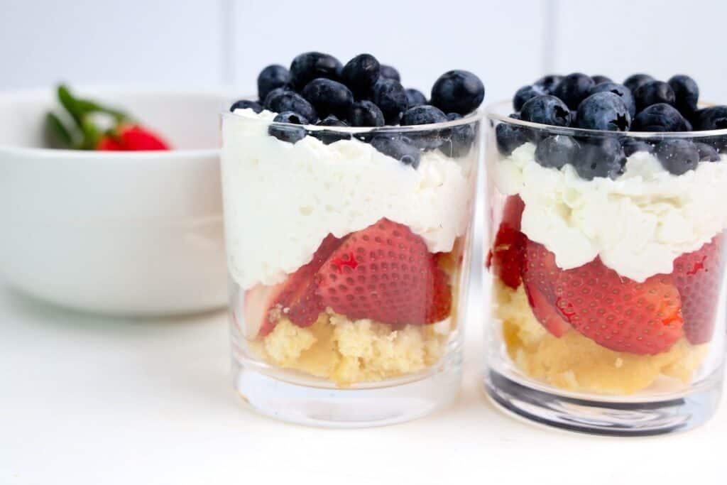Assembling dessert shells, strawberries, whipped cream, and blueberries in glasses to make 4th of July Trifles.