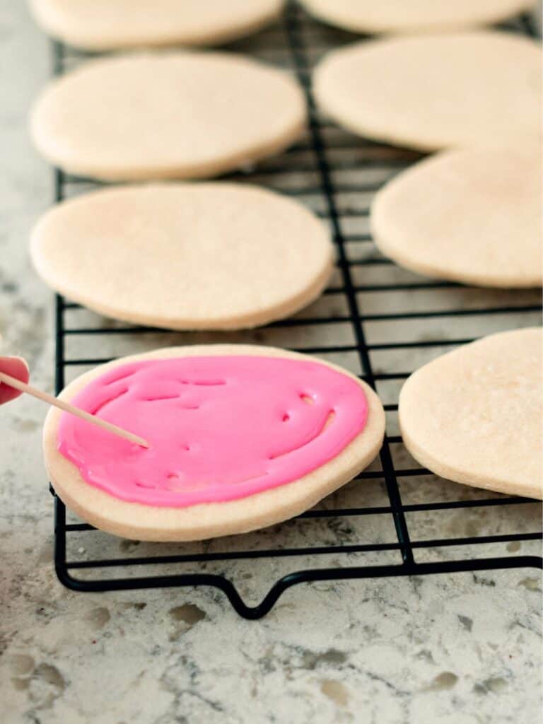 Icing Easter Sugar Cookies with pink icing on drying rack.