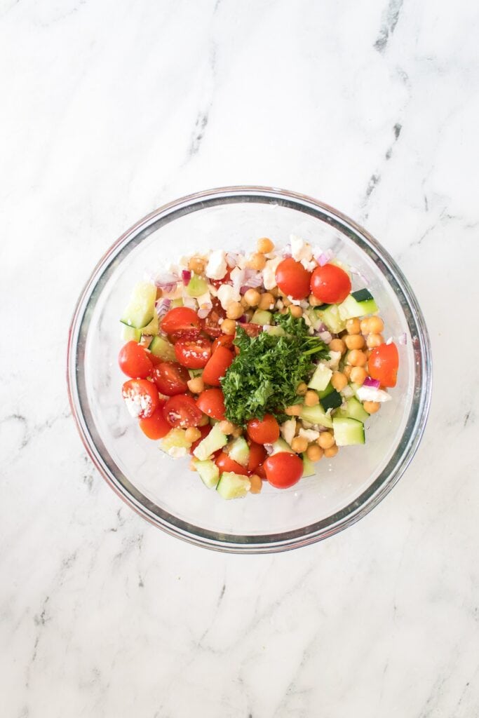 Chickpea Salad vegetable ingredients in glass bowl with parsley, overhead shot.