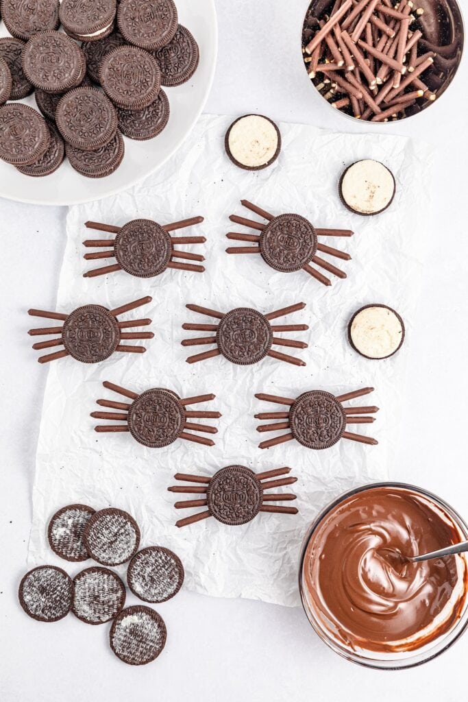 Oreo Spiders Halloween Cookies in process Oreo cookies, separated with Pocky sticks topped with Oreo cookie top, overhead shot.