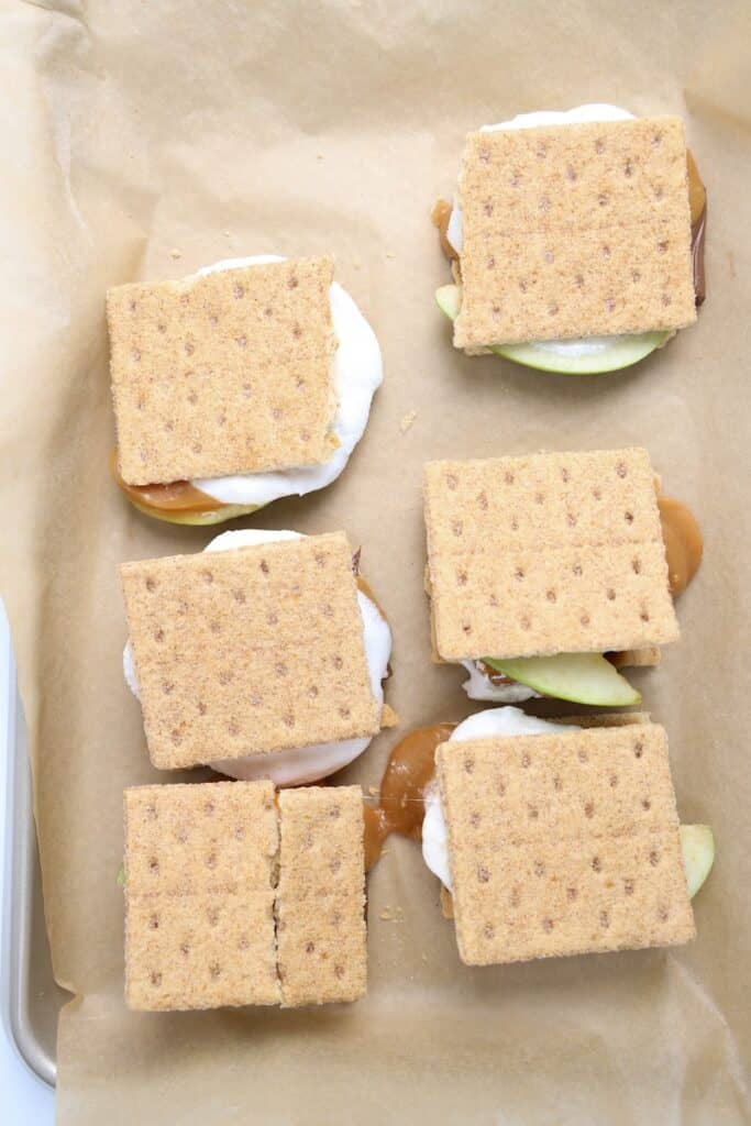Caramel Apple S’mores in process, layered graham crackers ready to bake on parchment lined baking sheet.