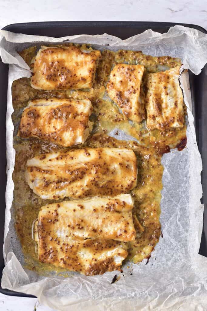 Maple Mustard Glazed Cod, cooked, on parchment lined baking pan.