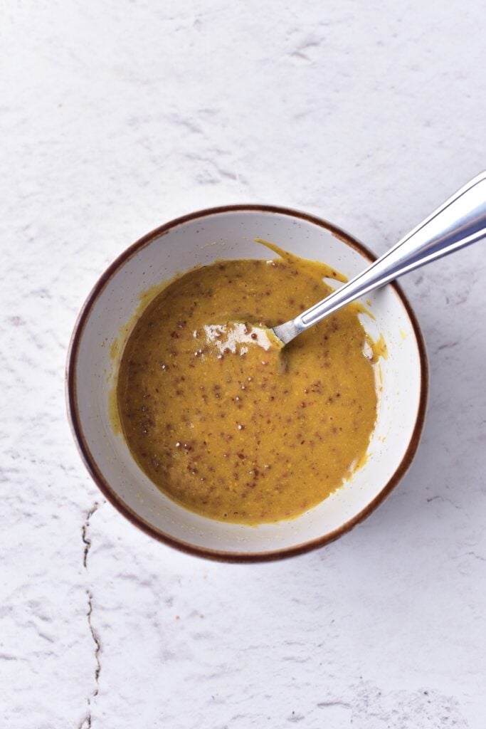 Maple Mustard Glazed Cod marinade ingredients with spoon in small mixing bowl, mixed.