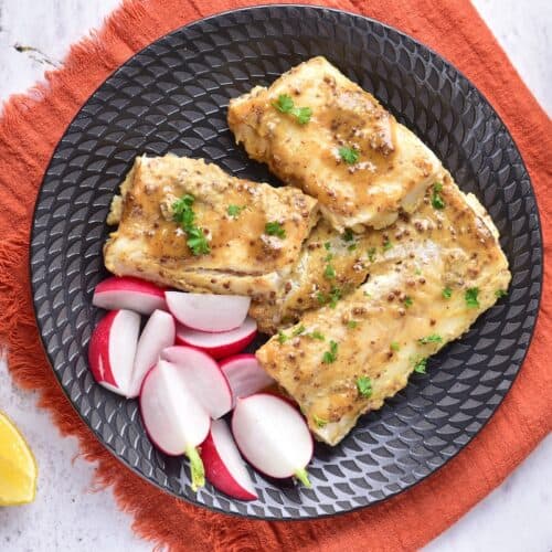 Maple Mustard Glazed Cod on black plate with radishes, overhead shot.