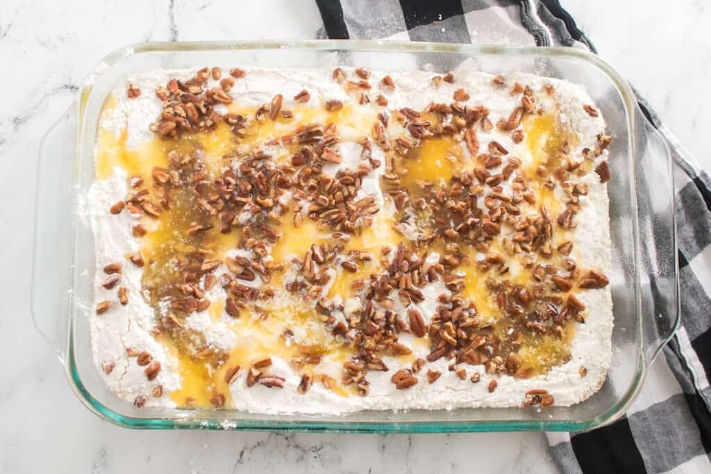 Pumpkin Crunch Cake, in process, melted margarine and pecans sprinkled on cake mix and batter in glass baking dish.