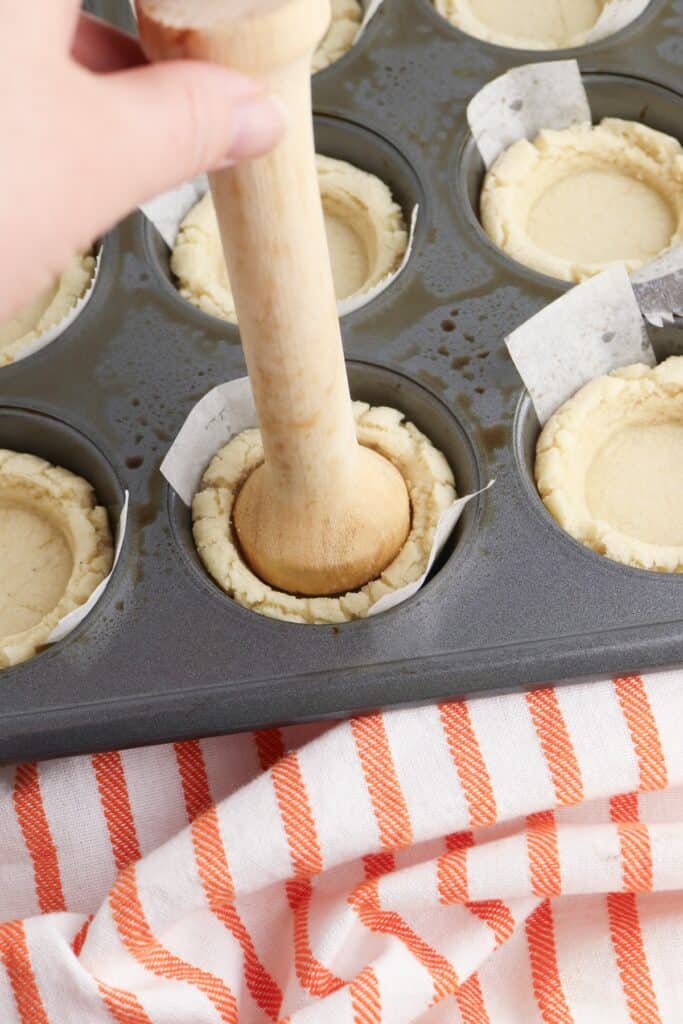 Pumpkin Pie Sugar Cookies, in process, flattening cookie dough in parchment lined muffin pan with tart tamper.