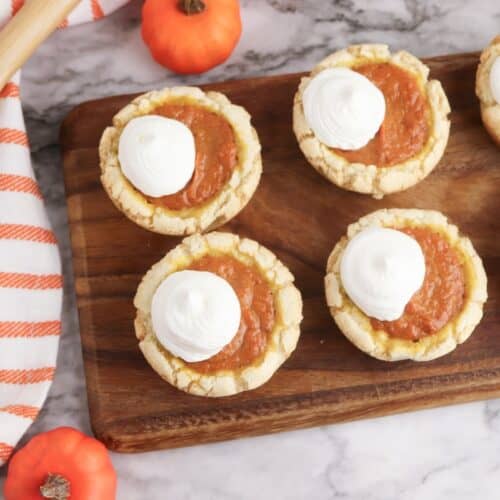 Pumpkin Pie Sugar Cookies on wooden cutting board with striped towel, overhead shot.