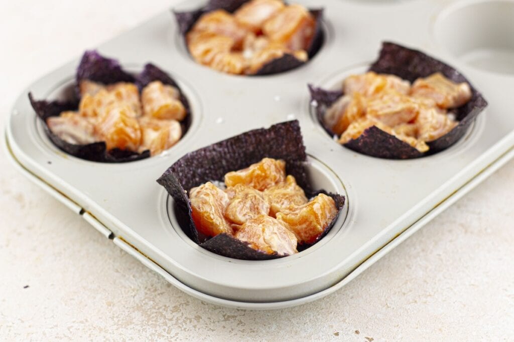 Baked Salmon Sushi Cups, in process, nori squares with cauliflower rice and marinated salmon in muffin pan.
