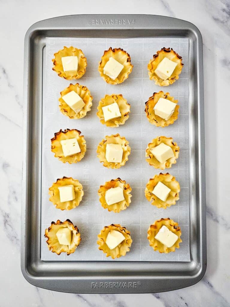 Cranberry and Walnut Brie Bites, in process, brie in phyllo shells on baking tray, overhead shot.