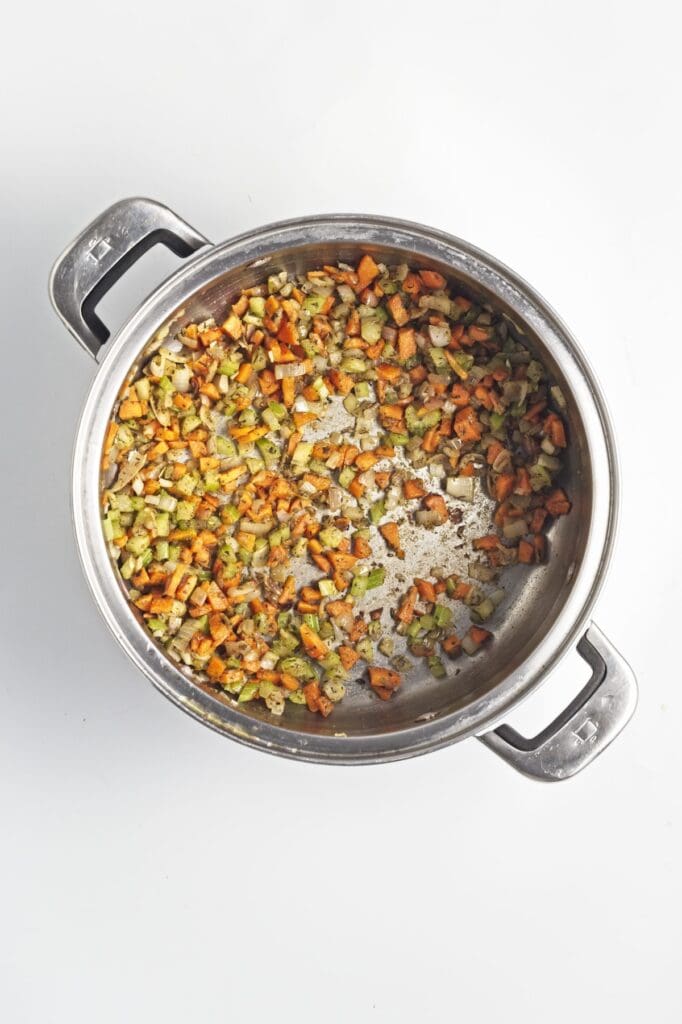 Creamy Mushroom Wild Rice Soup, in process, diced carrots, celery and onions with herbs, cooked in stock pot.