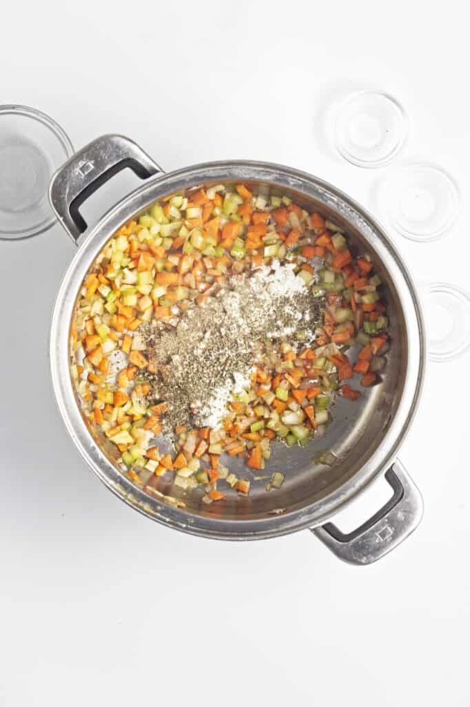 Creamy Mushroom Wild Rice Soup, in process, cooked diced carrots, celery and onions, with herbs in stock pot.