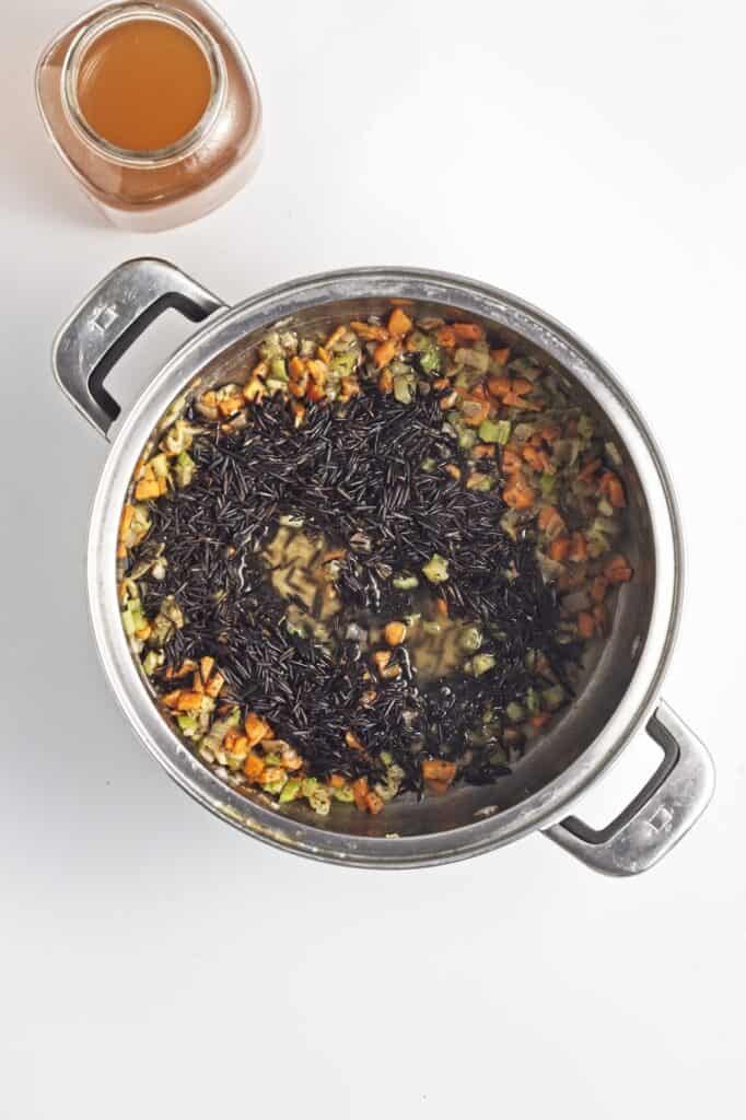 Creamy Mushroom Wild Rice Soup, in process, wild rice and broth added to vegetable mixture in pot.