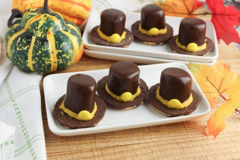 Fudge Stripe Pilgrim Hat Cookies on two white serving trays with fall gourds on wooden table.