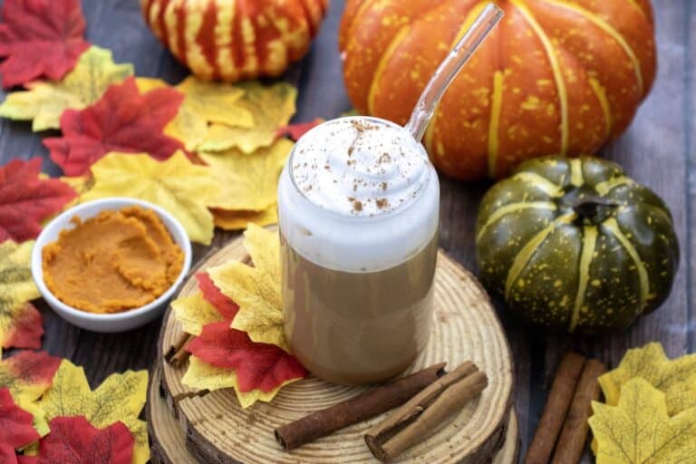 Homemade Pumpkin Spice Latte in glass with whipped cream and glass straw with autumn background.
