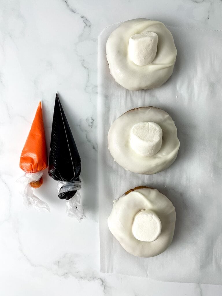 Melted Snowman Donuts, in process, orange and black icing and marshmallows attached to donuts.