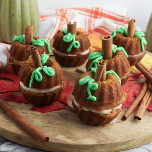 Mini Cream Cheese Pumpkin Cakes on wooden cutting board with cinnamon sticks.