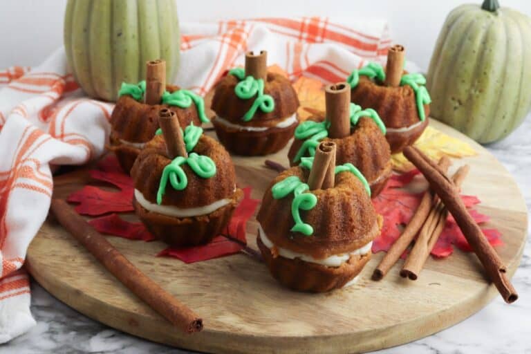 Mini Cream Cheese Pumpkin Cakes on wooden cutting board with cinnamon sticks.