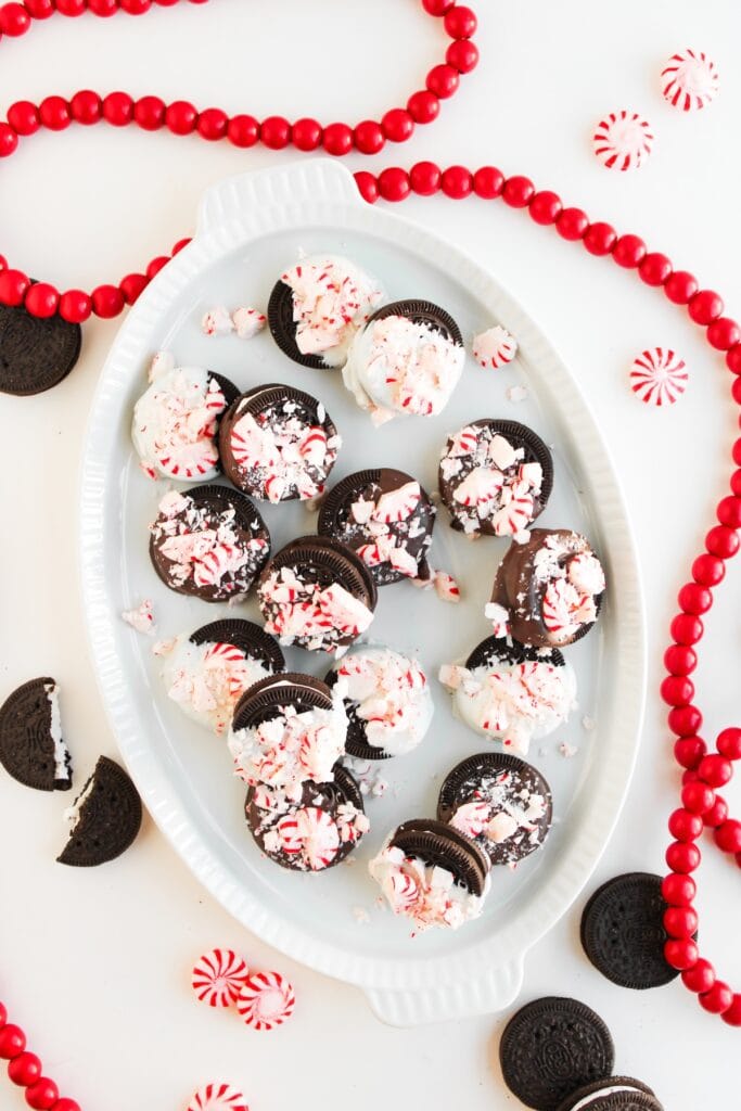 Peppermint Chocolate Covered Oreos on white serving plate surrounded by red beads, overhead shot.