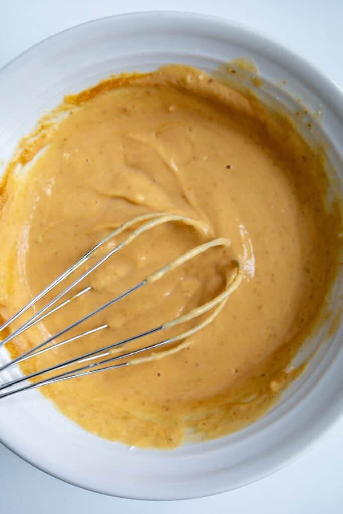 Pumpkin Cinnamon Rolls in process, frosting in bowl with whisk.