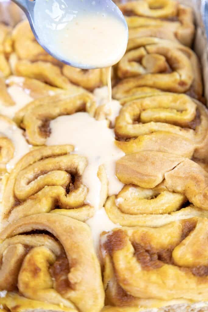 Pumpkin Cinnamon Rolls with frosting spooned over them, close-up.