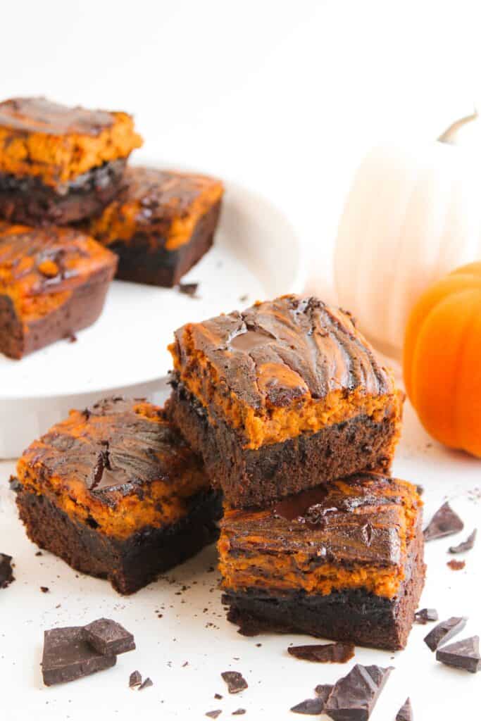 Pumpkin Spice Fudgy Brownies on white with chocolate pieces and mini pumpkin.