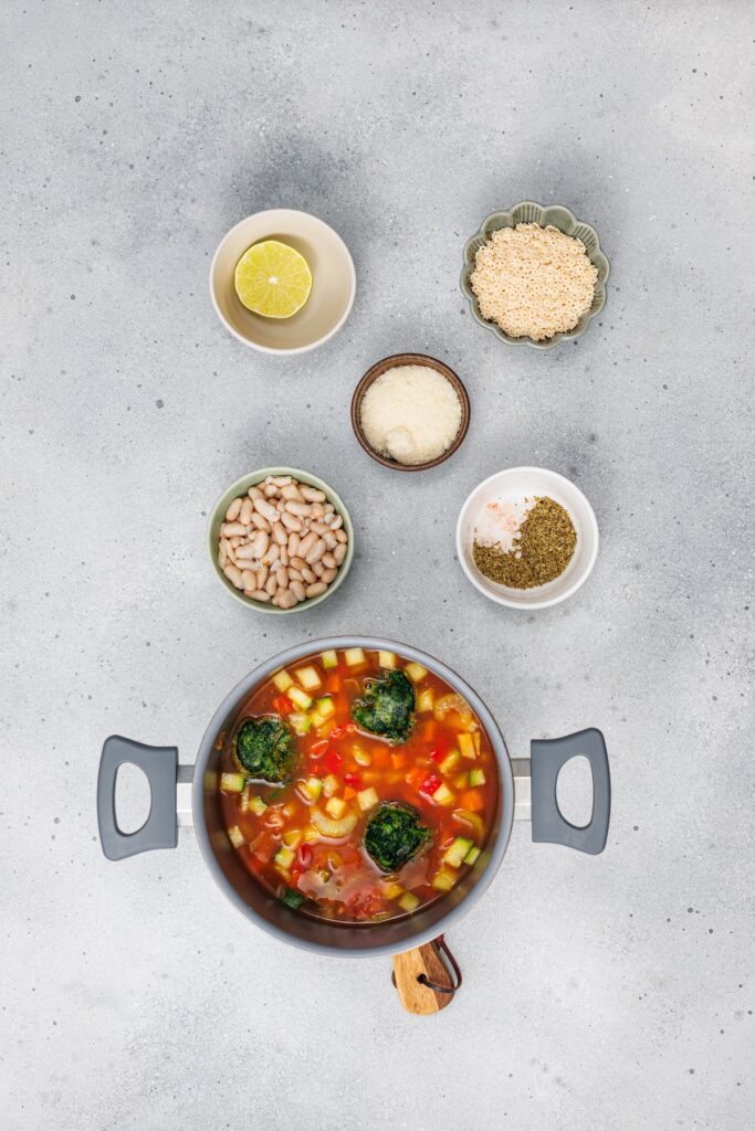 Veggie Minestrone Soup, in process, cooking tomatoes, frozen spinach, and vegetable broth in pot with other ingredients on the side.