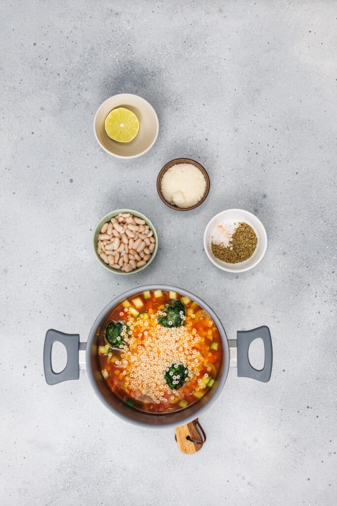 Veggie Minestrone Soup, in process, pasta added to pot with other ingredients on the side.