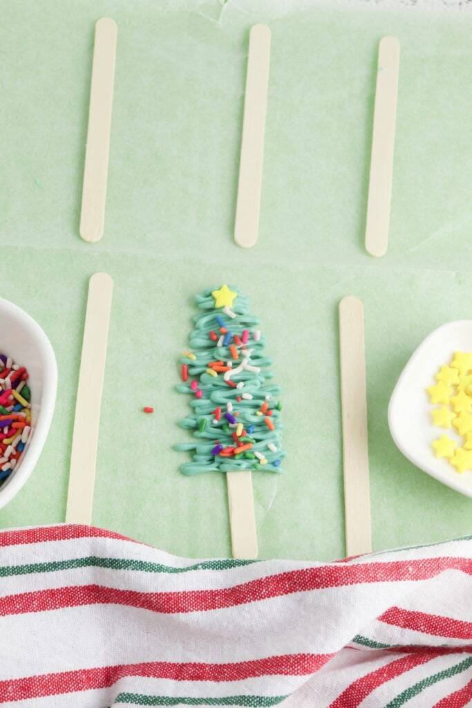 Christmas Tree Pops, in process, sprinkles added to green candy triangle on popsicle stick.