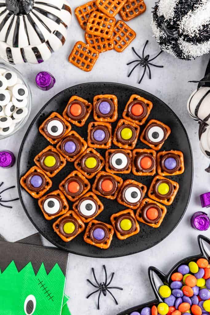 Halloween Rolo Pretzels on black plate with pretzels and M&M's and Halloween napkins.