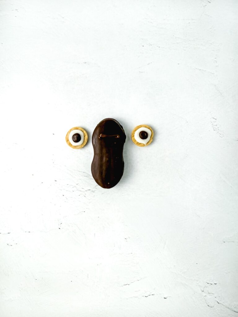 Nutter Butter Owl Cookies, in process, attaching eyes to chocolate-covered Nutter Butter.