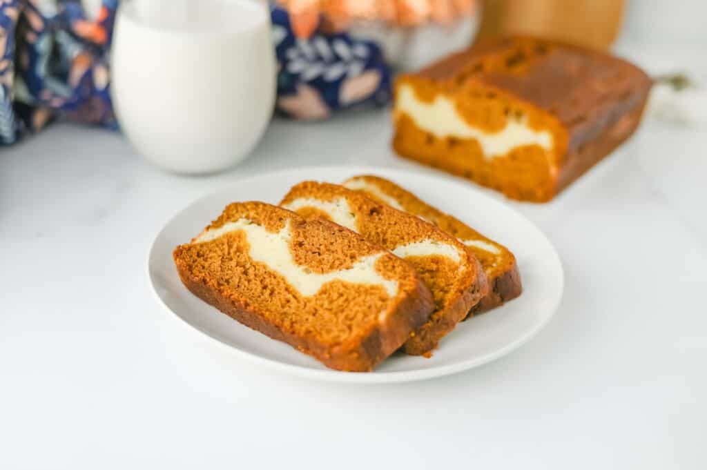 Pieces of Pumpkin Cream Cheese Bread on white plate with glass of milk.
