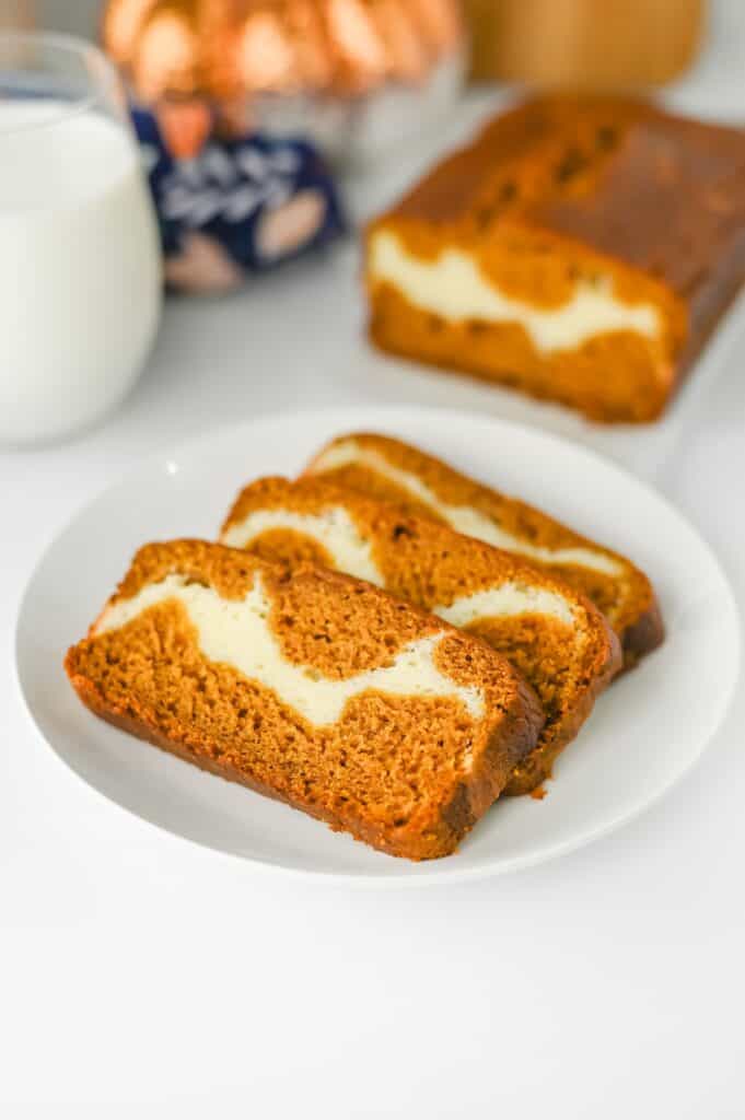 Pieces of Pumpkin Cream Cheese Bread on white plate with glass of milk.