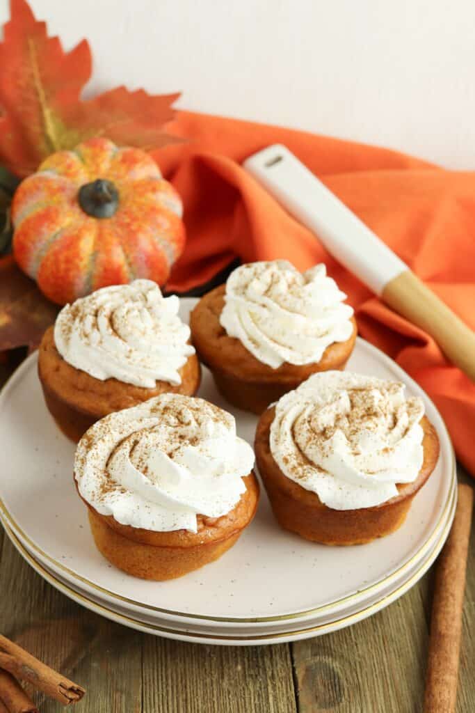 Four Pumpkin Pie Cupcakes on plate with orange towel and pumpkin background.