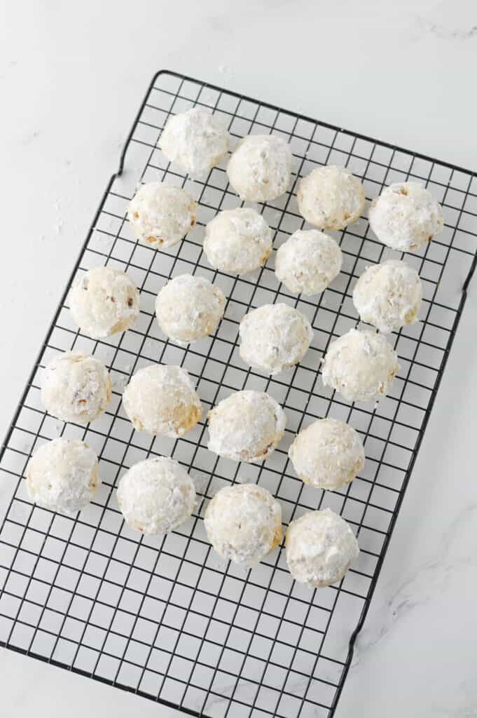 Pecan Snowball Cookies, in process, cookies on black wire cooling rack.