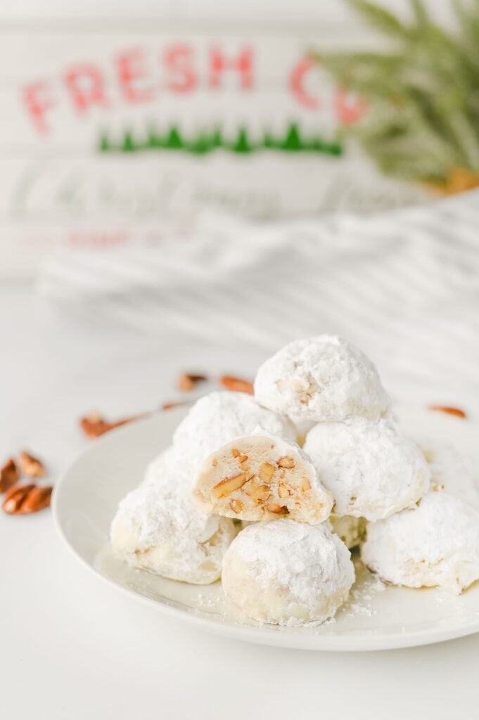 Pecan Snowball Cookies on white plate in kitchen surrounded by pecan pieces.